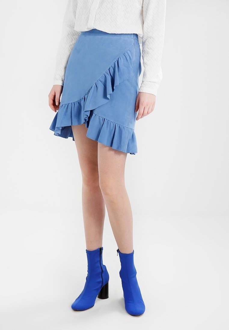 Mini jupe bleu volante en tissu doux et texturé. Présente un ourlet asymétrique et un design superposé. Associée à des bottines bleu vif.