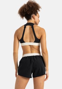 Zwarte sportbeha met brede bandjes en een contrasterende beige band, gecombineerd met zwarte shorts met een gathering op de witte tailleband.