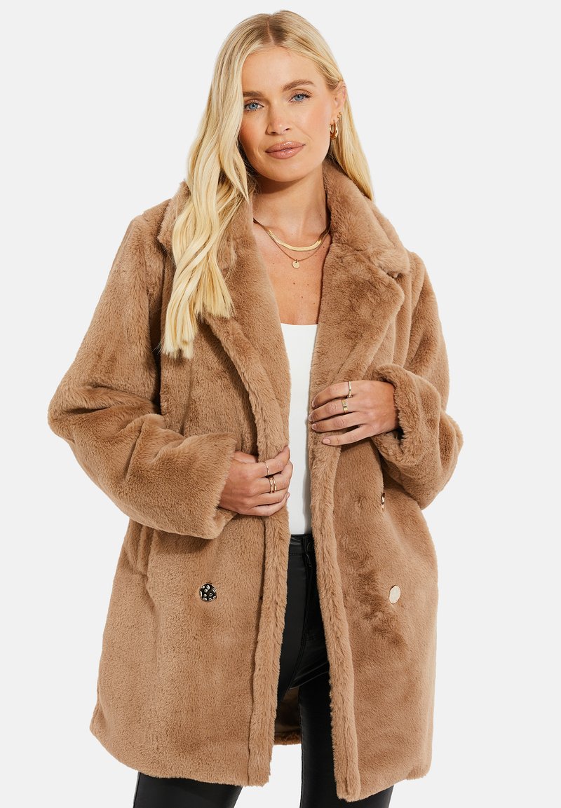 Manteau en fausse fourrure marron avec un col, des boutons sur le devant et deux poches latérales. Texture douce et coupe décontractée. Détails accentués par un logo.