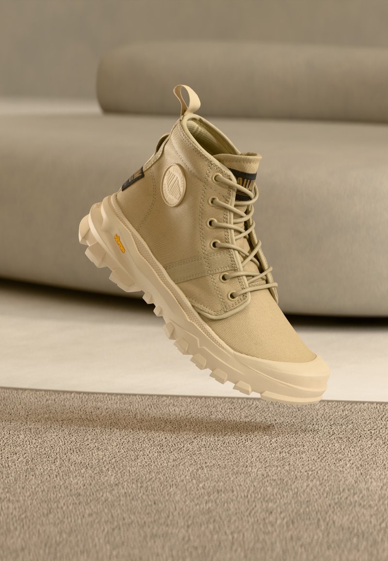 Bež visoke tenisice od platna, s okruglim detaljem logotipa, vezicama i robusnim đonom s vidljivim uzorcima za prianjanje.