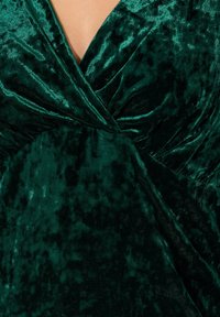Zielona aksamitna sukienka z krzyżującym się krojem, miękką fakturą i głębokim dekoltem w serek, z delikatnym połyskiem i nieregularnymi wzorami na całej powierzchni.