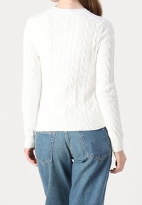Biały sweter w splot warkoczowy z prążkowanym dołem i mankietami, o klasycznym dekolcie w serek. Noszony z jeansami w kolorze niebieskim o wysokim stanie.