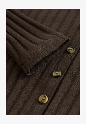 Brūna ribota auduma ar salocītu piedurkni un trim apaļām pogām dažādās krāsās, parādot tekstūru un apģērba detaļas.