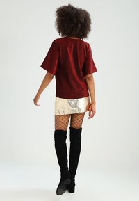Top corto de lentejuelas rojas con un ajuste relajado, combinado con una minifalda plateada metálica. La modelo lleva botas negras de muslo alto y medias de rejilla.