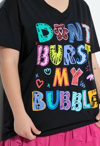 Maglietta nera a collo a V con testo colorato che legge "NON FAR SCOPPIARE LA MIA BOLLA." Il design include vari motivi e accenti giocosi.