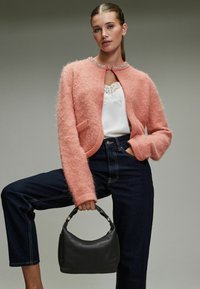 Pink fuzzy cardigan with a round neckline, featuring a decorative trim. Paired with dark jeans and a small black leather handbag.