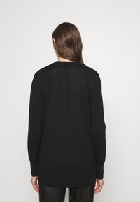 Musta pitkähihainen neule, jossa on pyöreä kaula-aukko, ribbitekniikalla tehdyt hihansuut ja helma, sekä kevyt, hieman kuviollinen kangas.