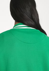 Sudadera verde con una textura suave, que presenta un cuello redondeado con rayas blancas, mostrando un color uniforme sin patrones adicionales.