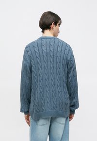 Πουλόβερ με πλέξη καλωδίων σε απαλό μπλε χρώμα. Διαθέτει υφή με μοτίβο, στρογγυλή λαιμόκοψη και χαμηλωμένους ώμους. Ριμπ τελείωμα και μανσέτες.