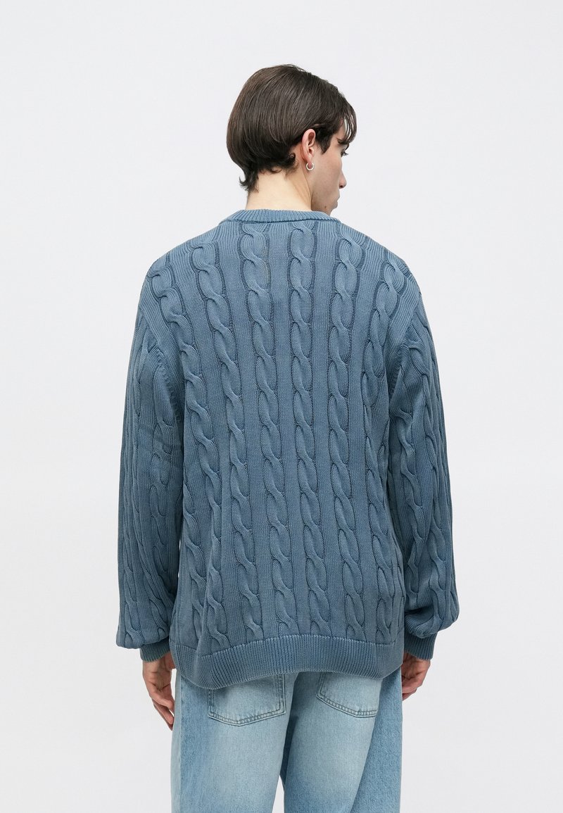 Trui met kabelgebreid patroon in zachtblauw. Voorzien van een gestructureerd patroon, een ronde halslijn en verlaagde schouders. Geribbelde tailleband en manchetten.