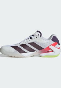 Baskets de sport blanches avec des rayures noires, cadre de soutien rouge au niveau du talon, section de semelle vert lime et tige en mesh, montrées du côté extérieur.