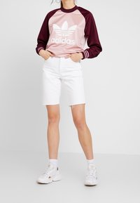Adidas långärmad tröja i rosa och vinrött med vitt logo, tillsammans med vita denimshorts med fransad fåll och vita sneakers.