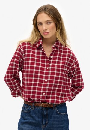 Chemise en flanelle à carreaux rouges et blancs avec un devant boutonné et un col, associée à un jean bleu et une ceinture tressée marron.