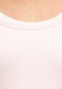 Κοντινή λήψη ενός ριμπ ύφανσης, ανοιχτό ροζ υφασμάτινου λαιμόκοψης σε ένδυμα, που δείχνει λεπτομέρειες ραφής και ανοιχτό χρώμα δέρματος από πάνω.