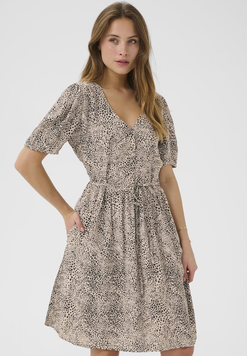 Robe à manches courtes beige avec un imprimé animal noir. Dotée d'un décolleté en V, d'une taille élastique et de poches latérales. Texture de tissu doux.
