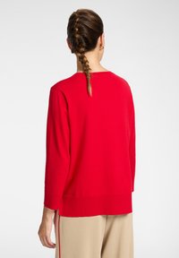 Jersey de algodón rojo con mangas largas, puños acanalados y un corte relajado. La parte trasera presenta un escote redondo y aberturas laterales en el dobladillo.