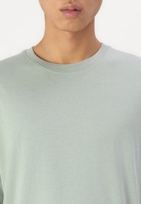 Lys grønn kortermet t-skjorte med rund hals laget av myk bomull, med en jevn tekstur og et enkelt, uten dekorasjoner design.