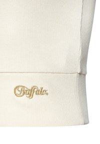 Cream-colored ribbed sweater with a fitted shape and gold embroidered "Buffalo" logo at the hem. Soft texture, minimalistic design.