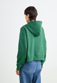 Green cropped hoodie with a adjustable hood, made of soft material. Features dropped shoulders and ribbed hem. Paired with light blue jeans.