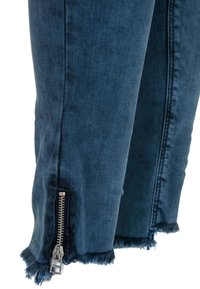 Dunkelblaue Denim-Jeans mit franstem Saum und silbernem Reißverschlussdetail am Knöchel. Glatte Textur mit sichtbaren Nähten entlang der Seite.