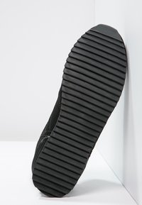 Chaussure de sport noire avec une semelle en caoutchouc texturé dotée de profondes rainures pour une meilleure adhérence. Tige en tissu tricoté et col rembourré pour plus de confort.
