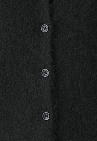 Μαύρη καφετί κάρντιγαν από μάλλινο ύφασ�μα με απαλή, υφαντή επιφάνεια και έξι ταιριαστούς στρογγυλούς κουμπιά κατά μήκος του μπροστινού μέρους.