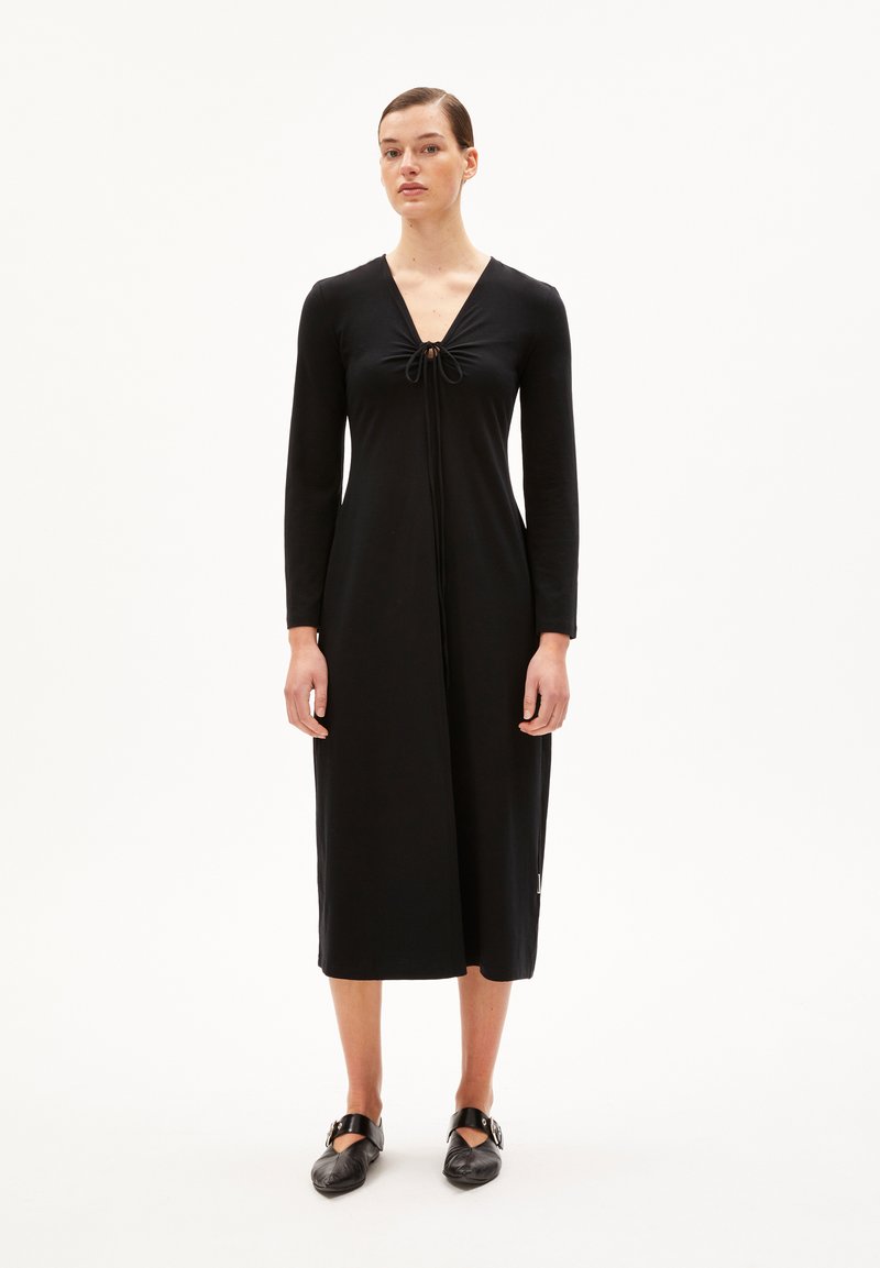 Schwarzes langärmliges Kleid mit tiefem V-Ausschnitt, gebundenem Detail an der Brust und gerader Midi-Silhouette. Hergestellt aus weichem, dehnbarem Material.