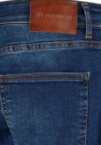 Jean en denim bleu foncé avec surpiqûres orange et un patch en cuir marron portant l'étiquette "2Y PREMIUM" au-dessus de la poche arrière.