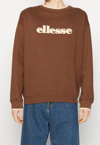 Hnědá mikina s žebrovaným kulatým výstřihem, se smetanově bílým vyšitým logem na přední části a kontrastními manžetami.