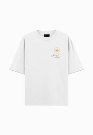 Wit oversized t-shirt met een klein gouden zonlogo en de tekst "Black Bananas" op de bovenste linkerborst.