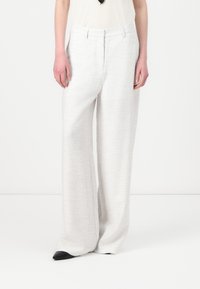 Light gray wide-leg trousers in textured fabric, featuring a structured waistband and crease details, paired with pointed black shoes.
