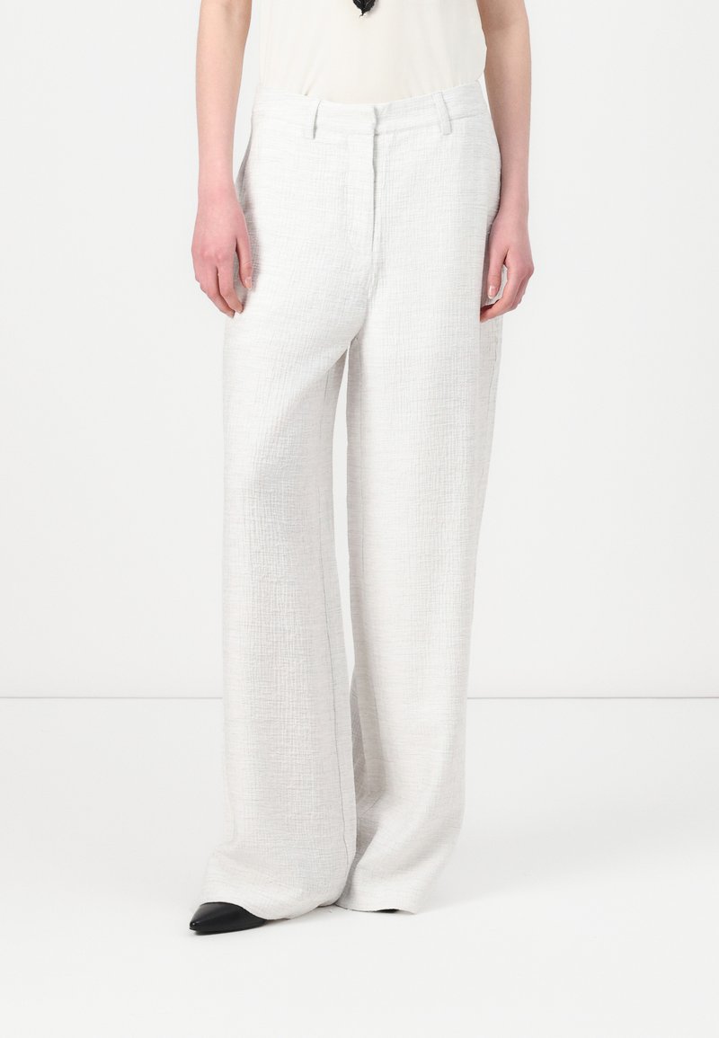 Pantalons larges gris clair en tissu texturé, dotés d'une taille structurée et de plis, assortis à des chaussures noires à bouts pointus.