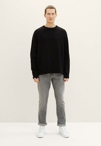 Suéter negro de punto con cuello redondo, combinado con jeans gris claro y zapatillas blancas. Diseño sencillo, corte relajado.