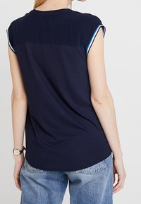 Top corto blu navy con orlo arrotondato, caratterizzato da un retro in un unico colore e piping a contrasto sulle spalle. Tessuto morbido e elasticizzato.