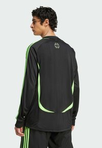 Camiseta deportiva de manga larga negra con detalles y rayas verdes, hecha de un material suave y ligero con un diseño ajustado.