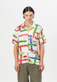 Short-sleeve button-up shirt featuring a multicolored patchwork design with various text, in white fabric with a relaxed fit.