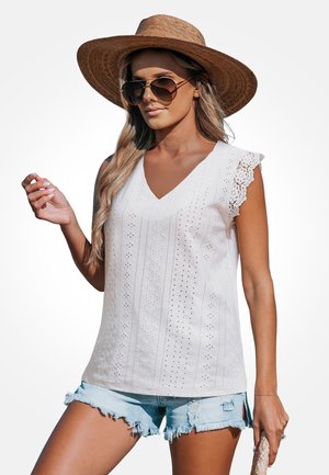 Biały top bez rękawów z dekoltem w kształcie litery V, ozdobiony koronkową lamówką na ramionach i wzorem ażurowym. Połączony z jasnymi szortami z denimu i dopełniony szerokim kapeluszem.