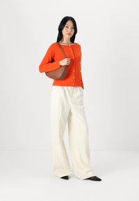 Orange cardigan with round neckline and buttons, paired with cream wide-leg trousers and black pointed-toe shoes. Brown shoulder bag.
