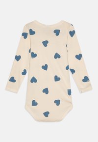 Body a maniche lunghe in morbido tessuto crema con stampa a cuori blu. Presenta una scollatura arrotondata e chiusura a pressione sul fondo per un facile indosso.