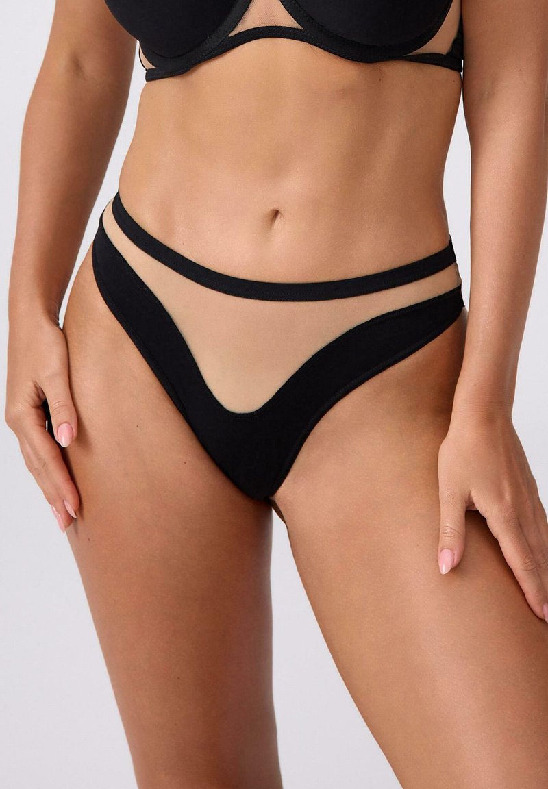 Czarne bikini dolne z przezroczystymi panelami, w kształcie litery V z przodu i cienkimi, czarnymi ramiączkami. Miękka tekstura w kontrastowym odcieniu do koloru skóry.