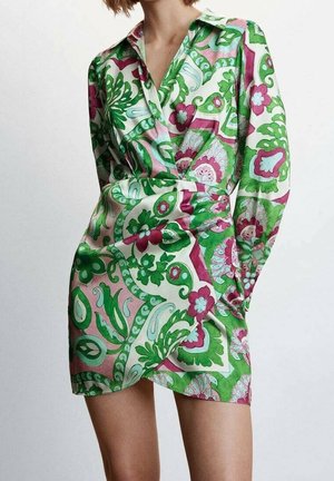 Femme portant une robe portefeuille en soie à manches longues avec un motif floral paisley vibrant en vert, rose et blanc.