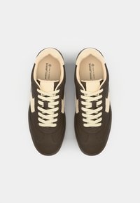 Braune vegane Sneaker mit einer hellbeigen Zehenkappe und seitlichen Akzenten. Ausgestattet mit weißen Schnürsenkeln und einem strukturierten Obermaterial. Minimalistisches Design.
