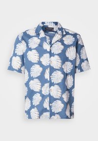 Chemise bleue à manches courtes avec boutons, motif de feuilles tropicales blanches et col, suspendue sur un fond blanc uni.