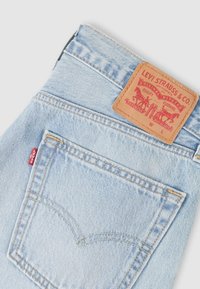 Φωτεινά γαλάζια τζιν από ντένιμ με δερμάτινο πλακίδιο που φέρει κόκκινα και μαύρα γραφικά, διπλή ραφή και μια μικρή κόκκινη ετικέτα λογότυπου στην πίσω τσέπη.