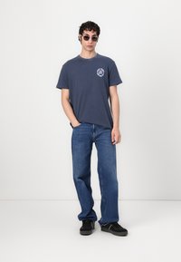 Marineblå bomull T-skjorte med rund hals og grafisk trykk på brystet, kombinert med løstsittende blåjeans og svarte sko.