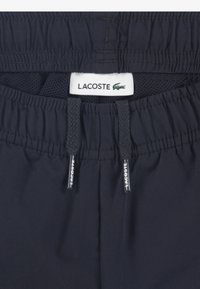 Σορτς με ελαστική μέση σε ναυτικό μπλε χρώμα και ρυθμιζόμενα κορδόνια, με επένδυση από δίχτυ και ετικέτα με το λογότυπο Lacoste. Ομαλή υφή υφάσματος.