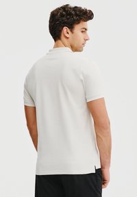 Biała koszulka polo z krótkim rękawem, z klasycznym kołnierzykiem, bocznymi rozcięciami i gładką fakturą, zaprojektowana w minimalistycznym stylu.