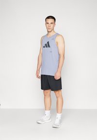 Lilla ermeløs treningssinglet med svart logo, kombinert med svarte shorts og lysegrå treningssko. Enkelt og funksjonelt design.