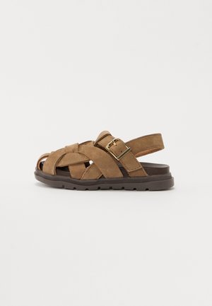 Brown suede sandals featuring a woven strap design, adjustable buckle, open-toe structure, and a textured rubber sole.