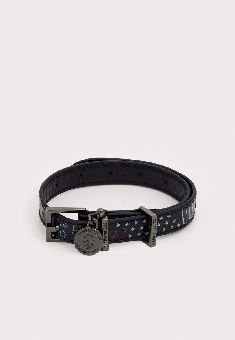 Pulsera de cuero negro con hebilla de plata y patrón de estrellas, que presenta un charm circular grabado con una calavera y el texto "Zadig & Voltaire".